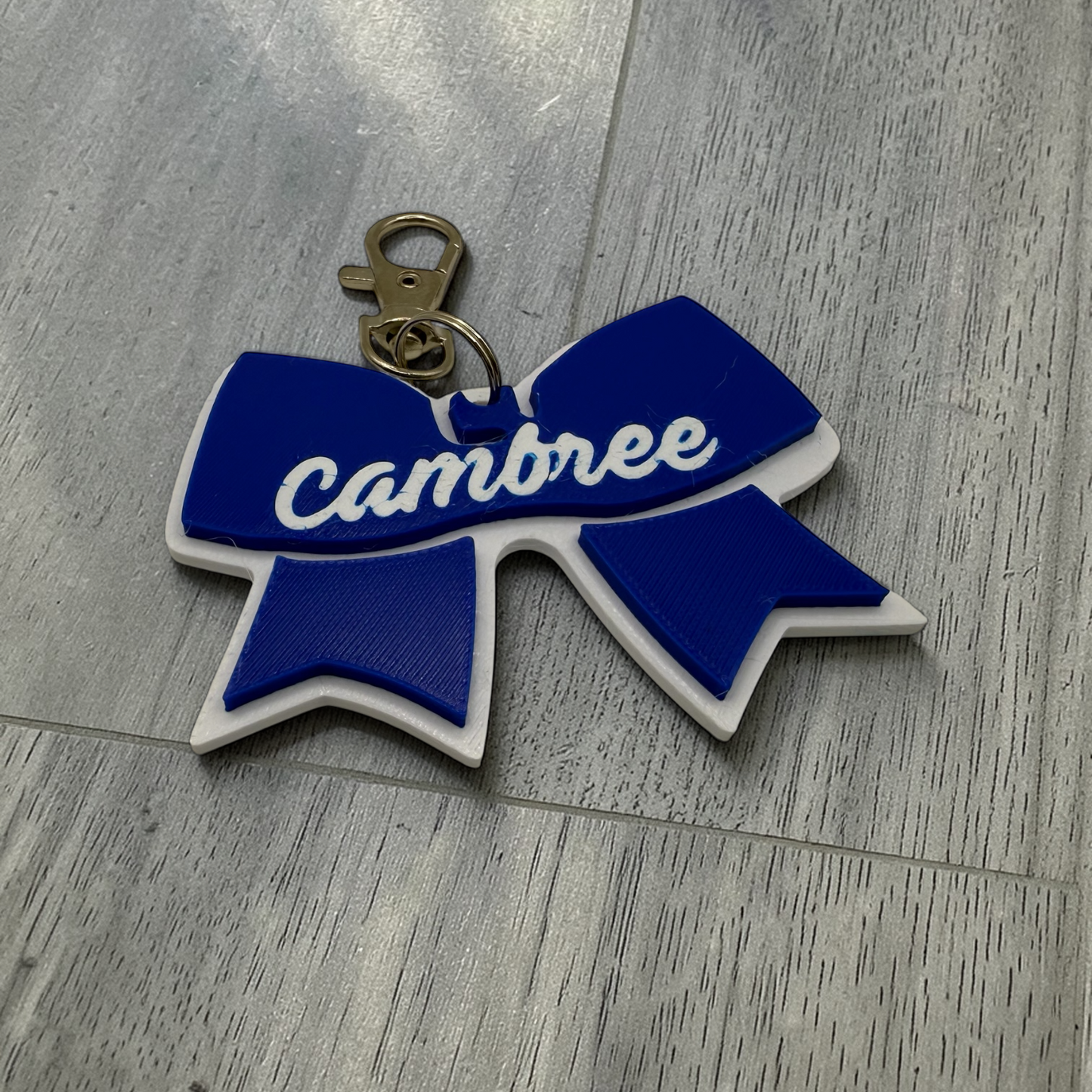 Blue and white bow-shaped keychain with 'cambree' text on a wooden surface