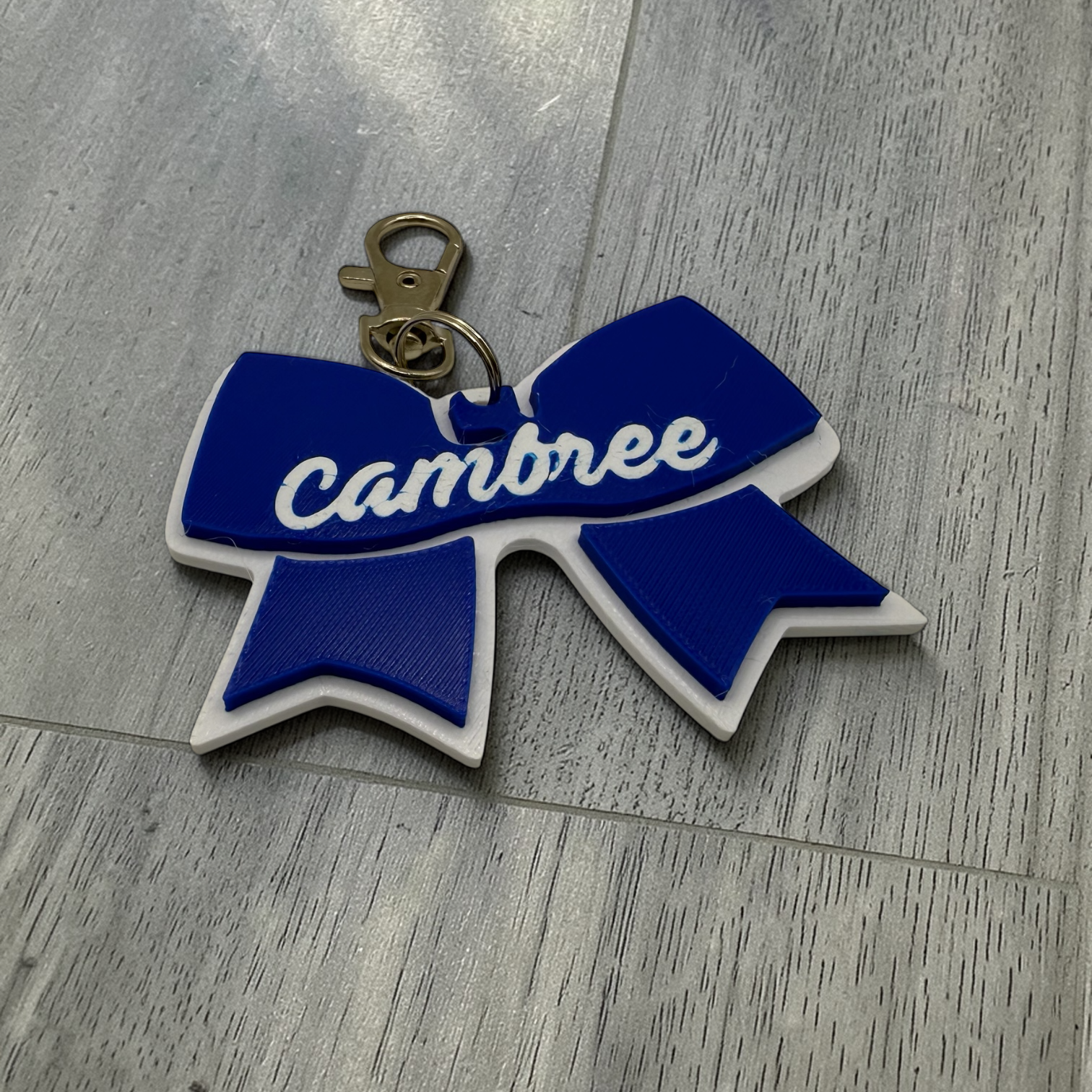 Blue and white bow-shaped keychain with 'cambree' text on a wooden surface